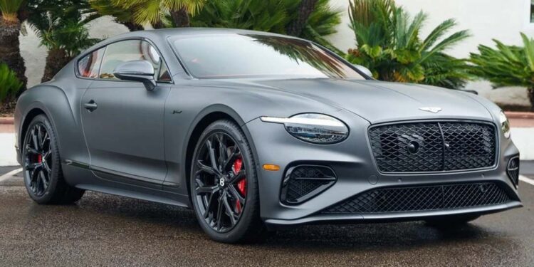 A sleek matte gray luxury sports coupe in stealth mode is parked on wet pavement, framed by palm trees and lush greenery.
