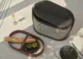 A modern Hyde Picnic Collection basket set on a table with a glass of champagne, a plate with two green tomatoes, and a baguette, under soft daylight—perfect for stylish outdoor living.