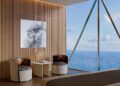 Modern hotel room with two chairs and a small table by a large window overlooking the ocean, featuring wooden panel walls and a contemporary painting, inspired by the sleek luxury of Bentley Residences Miami.