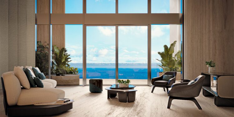 Modern penthouse living room with large floor-to-ceiling windows, beige sofas, elegant chairs, potted plants, and a stunning ocean view under a blue sky—an exquisite example of Miami real estate at Bentley Residences Miami.