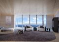 Modern penthouse bedroom suite with floor-to-ceiling windows, ocean view, circular seating area, large rug, neutral tones, and contemporary decor at Bentley Residences Miami.