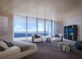 Modern penthouse bedroom with floor-to-ceiling windows, ocean view, two round chairs, a bed, abstract wall art, and a cabinet on a dark carpeted floor in the exclusive Bentley Residences Miami, listed at $37.5M.