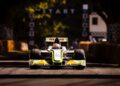 A Formula 1 car drives on a tree-lined racetrack, approaching the start line with barriers and checkered flags in the background, celebrating 75 Years of F1 excitement.