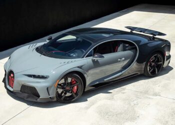 A grey Bugatti Chiron hypercar is parked on a concrete surface in bright daylight.