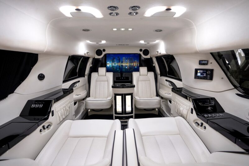 Interior for luxury limousine cars with white leather seats, surrounding lighting, large screen, control panels, and bright black accents - a unique creation that stands out between cars designated for sale.