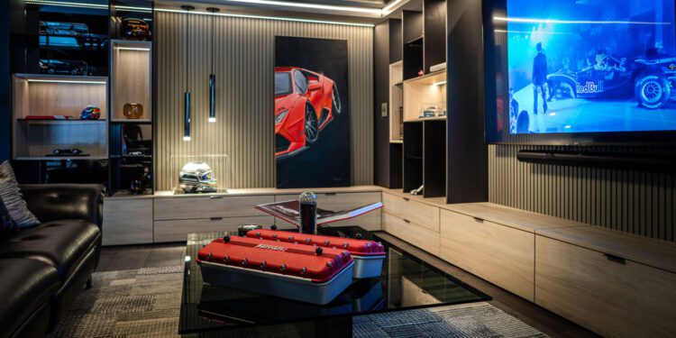 Modern entertainment room with a large wall-mounted TV showing a racecar, a black leather sofa, car-themed decor, and a glass coffee table displaying automotive items—perfect for Palm Beach luxury car collectors or CollectionSuites enthusiasts.