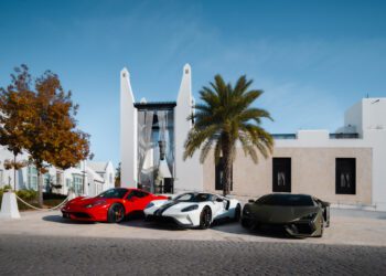Three luxury sports cars—a red, a white, and a dark green—are parked side by side in front of a modern white building at Alys Beach, capturing The Art of the Drive beneath swaying palms and a clear blue sky.