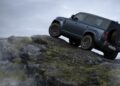 A blue Land Rover Defender Refreshed climbs over a rocky hill in a cloudy outdoor setting, showing off what's new for 2026.