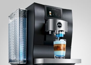 The JURA Z10 in a new color dispenses a beautifully layered latte into a clear glass, showcasing its modern automatic features, sweet enhancement technology, digital display, and transparent water reservoir.