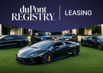 Four luxury black cars are parked on a green lawn in front of a building, with a duPont Registry Leasing banner above them.