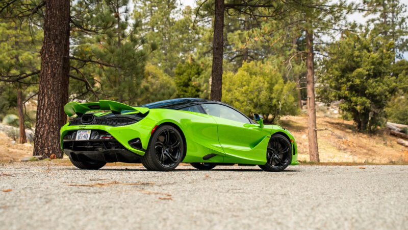A bright green sports car with black accents is parked on a paved area surrounded by trees and natural scenery.