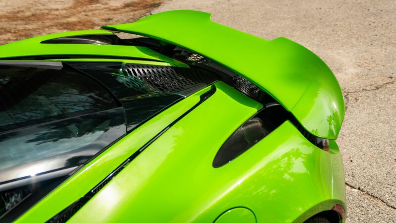 Close-up of a green sports car’s rear wing and engine cover, showing aerodynamic details and glossy paint under daylight.