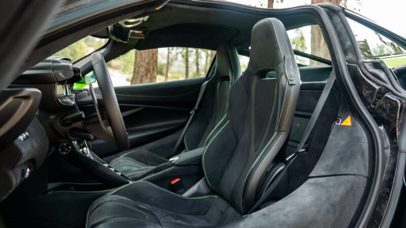 The photo shows the interior of a sports car with black and dark gray bucket seats, visible stitching, and a sleek dashboard.