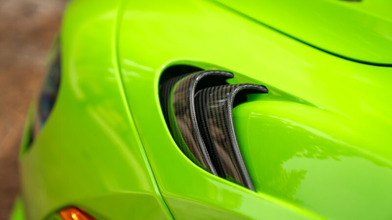 Close-up of a green sports car's body with a focus on black carbon fiber air vents.