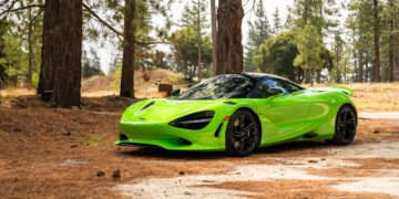 A bright green sports car is parked on a dirt path surrounded by tall pine trees in a forested area.