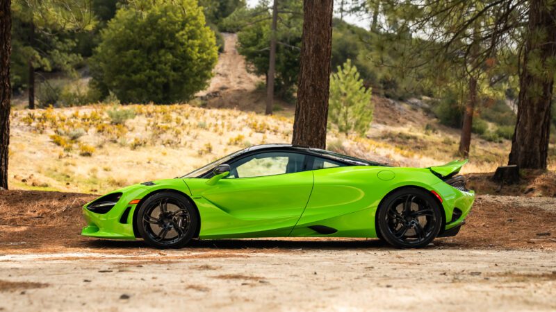 A bright green sports car parked on a dirt area surrounded by trees and greenery.