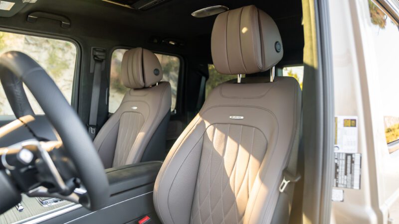 Front seats of a modern vehicle featuring brown leather upholstery, quilted pattern design, and visible headrests, with sunlight entering through the window.