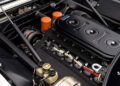 Close-up view of a classic 365 GTB/4 Daytona engine compartment at Ferrari Beverly Hills, highlighting the engine block, orange oil filters, electrical wiring, and various mechanical components.