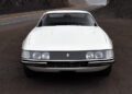 Front view of a classic white 365 GTB/4 Daytona sports car parked on an empty road with rocky hills in the background, reminiscent of the timeless elegance celebrated at Ferrari Beverly Hills.
