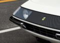 Close-up of the front end of a white Ferrari 365 GTB/4 Daytona, showing a headlight, Ferrari emblem, black grille, and bumper detail on an asphalt surface—captured at Ferrari Beverly Hills.