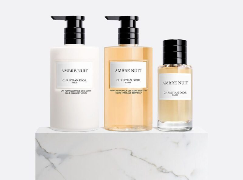 Three Ambre Nuit Christian Dior Paris body care products, including lotion, liquid soap, and perfume, are arranged on a white marble surface—a luxurious addition to any Father’s Day Gift Guide by duPont REGISTRY.