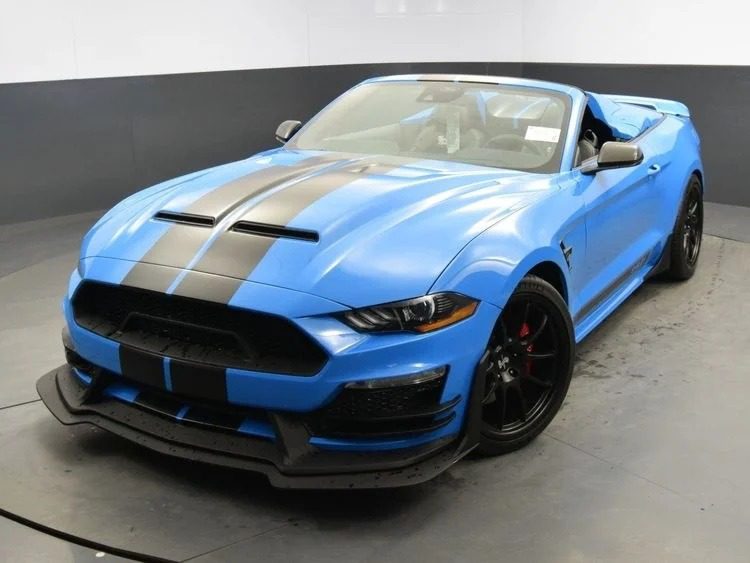 A blue convertible sports car with black racing stripes, black rims, and a rear spoiler is parked indoors on a gray garage floor—a stunning example of unique cars.