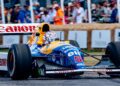A blue and yellow Formula 1 race car with Canon and Renault branding speeds down the track at the Festival of Speed, as a crowd watches behind barriers, celebrating 75 Years of F1.