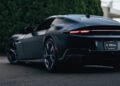A matte black Ferrari 12Cilindri sports car with 819HP is parked on pavement, viewed from the rear left side, tail lights illuminated and trees in the background—presented by Miller Motorcars.