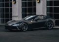 A matte black Ferrari 12Cilindri, boasting 819HP, is parked in front of a building with large glass-paneled garage doors and wall-mounted lights at Miller Motorcars.