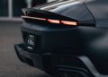 Rear view of a black 12Cilindri sports car with illuminated LED tail lights and a visible license plate holder on an outdoor pavement, showcased by Miller Motorcars.
