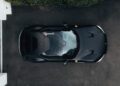 Overhead view of a matte black Ferrari 12Cilindri sports car with 819HP, parked on dark pavement beside greenery and a white structure at Miller Motorcars.