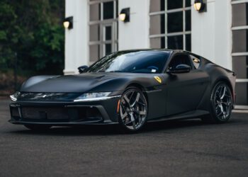 A matte black Ferrari 12Cilindri, boasting 819HP, is parked in front of a white building with large windows and exterior lights—a stunning showcase from Miller Motorcars.