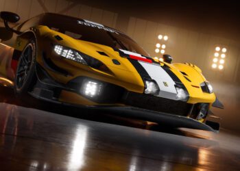 A yellow Ferrari 296 GT3 Evo race car with black and white striping is parked indoors under bright lights, viewed from a low front angle, capturing the spirit of the 24 Hours Of Spa.