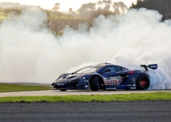A black Red Bull Drift Car drifts on a track at the Monterey Motorsports Festival, producing a large cloud of white smoke from its rear tires.