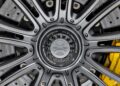 Close-up of a silver alloy wheel with center lock mechanism and visible brake disc; yellow Porsche brake caliper in background, echoing the high-performance style of the Gunther Werks Goes Modern: Meet GW9’s Carbon-Clad 992 Turbo S.