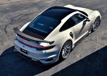 A silver sports car with a large rear spoiler, inspired by Gunther Werks Goes Modern: Meet GW9’s Carbon-Clad 992 Turbo S, is parked on an asphalt surface and viewed from above at an angle.