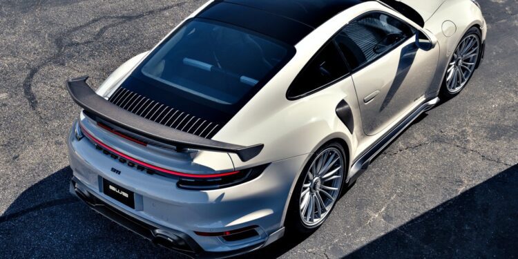 A silver sports car with a large rear spoiler, inspired by Gunther Werks Goes Modern: Meet GW9’s Carbon-Clad 992 Turbo S, is parked on an asphalt surface and viewed from above at an angle.