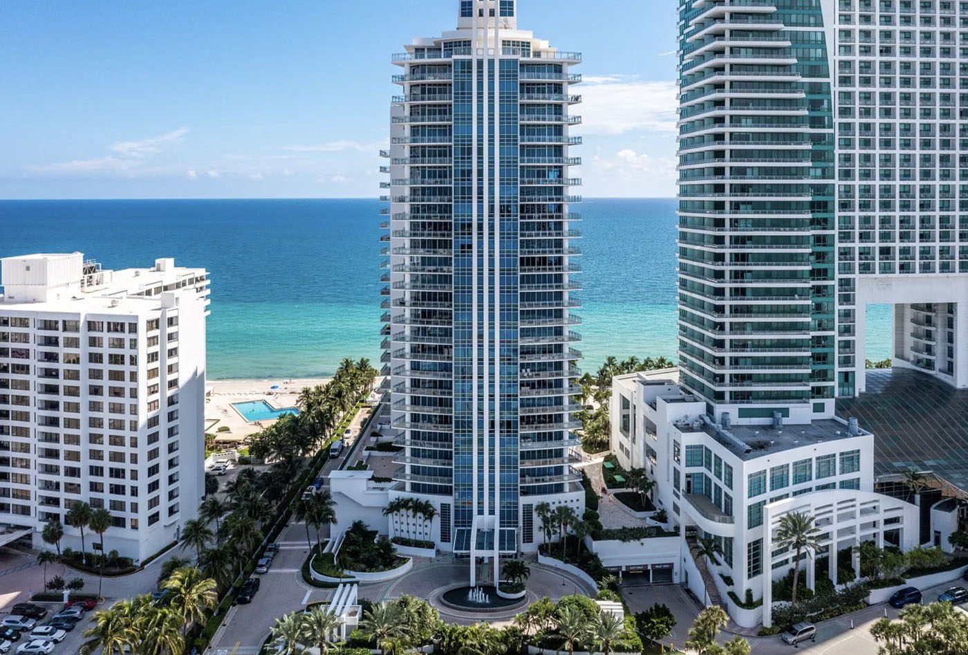 High-rise beachfront condominium building with balconies, flanked by other tall buildings, overlooking a pool and the ocean—offering unique opportunities often featured through CWS Marketing Group under a clear sky.
