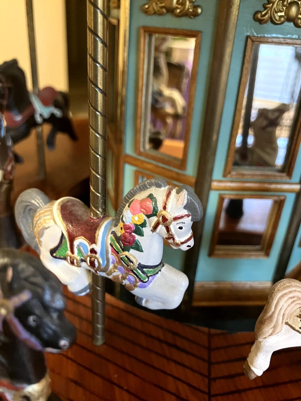 Close-up of a carousel horse figurine with colorful painted details, set against a background featuring mirrors and decorative gold accents.