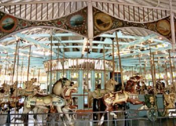 Antique carousel with elaborately painted horses and a decorative canopy under a roofed structure.