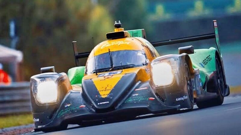 A green and yellow prototype race car drives on a racetrack with its headlights on, as Ferrari clinches a historic third straight Le Mans victory while Porsche denies a podium sweep.