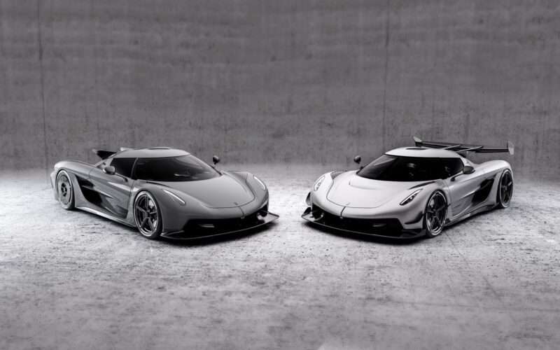 Two silver Koenigsegg hypercars are parked side by side in a minimalistic, concrete-walled indoor space, both flaunting track-focused, sleek aerodynamic designs and low profiles.