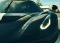 Close-up of the front left side of a dark-colored sports car with its headlight on, showcasing aerodynamic lines—meet the Farewell Jesko: Enter Track-Focused 1625 HP Koenigsegg Sadair's Spear, with striking reflections on the hood.
