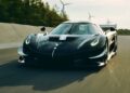 A black Koenigsegg Sadair's Spear sports car drives at speed on a paved road, with wind turbines and trees in the background—farewell Jesko, as the new 1625 HP track-focused masterpiece takes the lead.