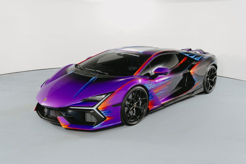 A Lamborghini Revuelto in a studio, featuring a glossy purple Opera Unica paint job with striking orange and blue accents, created to celebrate the 60th Anniversary.