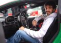 A man in a white hoodie and jeans sits in the driver's seat of a green sports car, smiling at the camera, with a racing helmet beside him—wondering what two-time MotoGP champ Francesco Bagnaia makes of the Lamborghini Temerario.