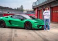 A man stands next to a bright green sports car, reminiscent of what two-time MotoGP champ Francesco Bagnaia makes of the Lamborghini Temerario, parked in front of red garage doors at a race track.