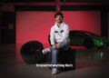 A man in a white hoodie sits on stacked tires in a garage, with a green sports car glowing under red lighting. Text on screen reads, "I'd never felt anything like it—what two-time MotoGP champ Francesco Bagnaia makes of the Lamborghini Temerario.