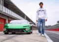 A man in a white hoodie and jeans walks on a racetrack next to a green sports car parked near red garages, evoking the style of What Two-Time MotoGP Champ Francesco Bagnaia Makes Of The Lamborghini Temerario.
