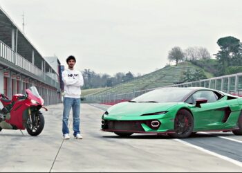 A person stands between a red motorcycle and a green sports car on a racetrack, echoing what two-time MotoGP champ Francesco Bagnaia makes of the Lamborghini Temerario, with empty stands and overcast skies in the background.